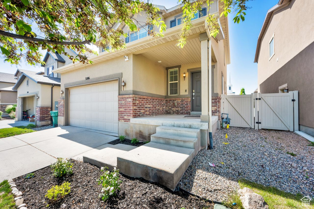 View of property featuring a gate, stucco siding, a garage, concrete driveway, and brick siding