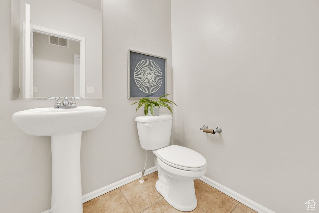 Half bathroom featuring baseboards, toilet, tile patterned floors, and a sink