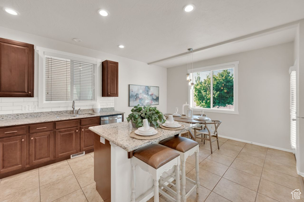 Kitchen featuring a sink, light tile patterned floors, light stone counters, a kitchen island, and a breakfast bar