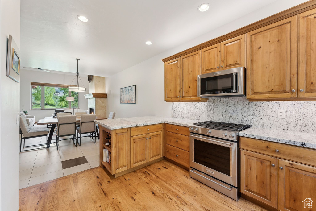 Kitchen with stainless steel appliances, a peninsula, tasteful backsplash, light stone counters, and recessed lighting