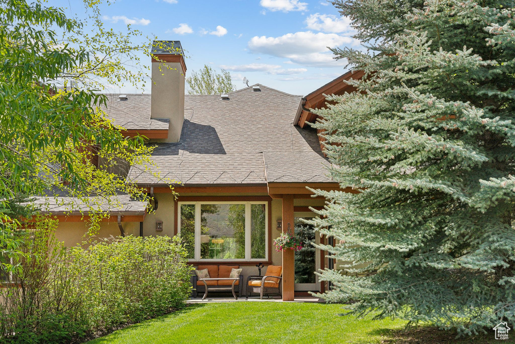 Back of property featuring outdoor lounge area, a shingled roof, a yard, a chimney, and stucco siding