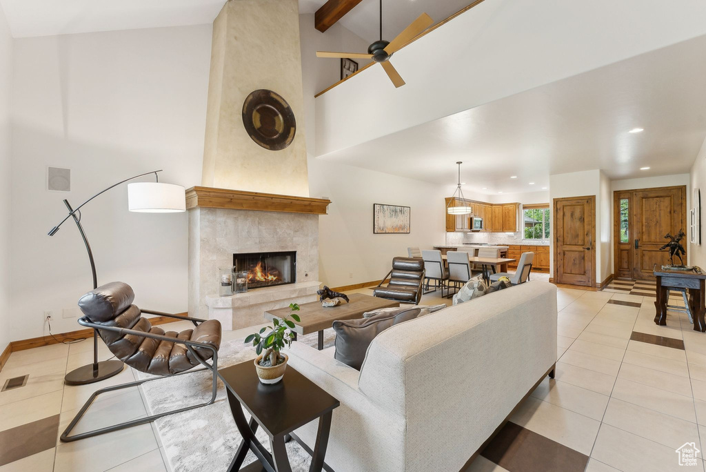 Living room with baseboards, light tile patterned flooring, ceiling fan, a high end fireplace, and high vaulted ceiling