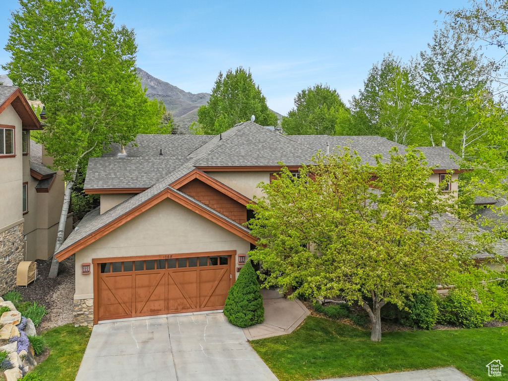 View of front of home with a shingled roof, stone siding, stucco siding, concrete driveway, and a mountain view