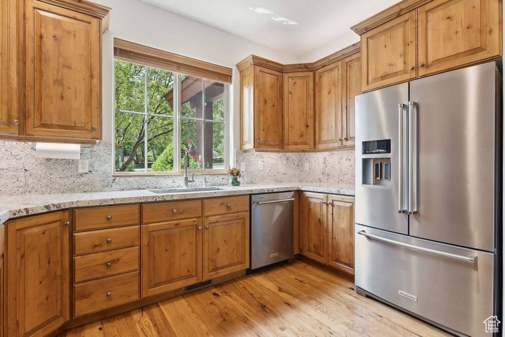 Kitchen featuring appliances with stainless steel finishes, a sink, decorative backsplash, light stone counters, and light wood-type flooring