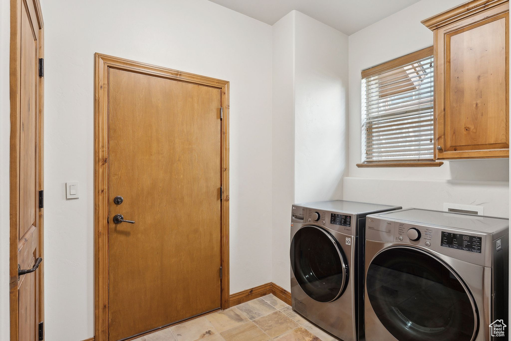 Clothes washing area with cabinet space, separate washer and dryer, baseboards, and light stone finish floors