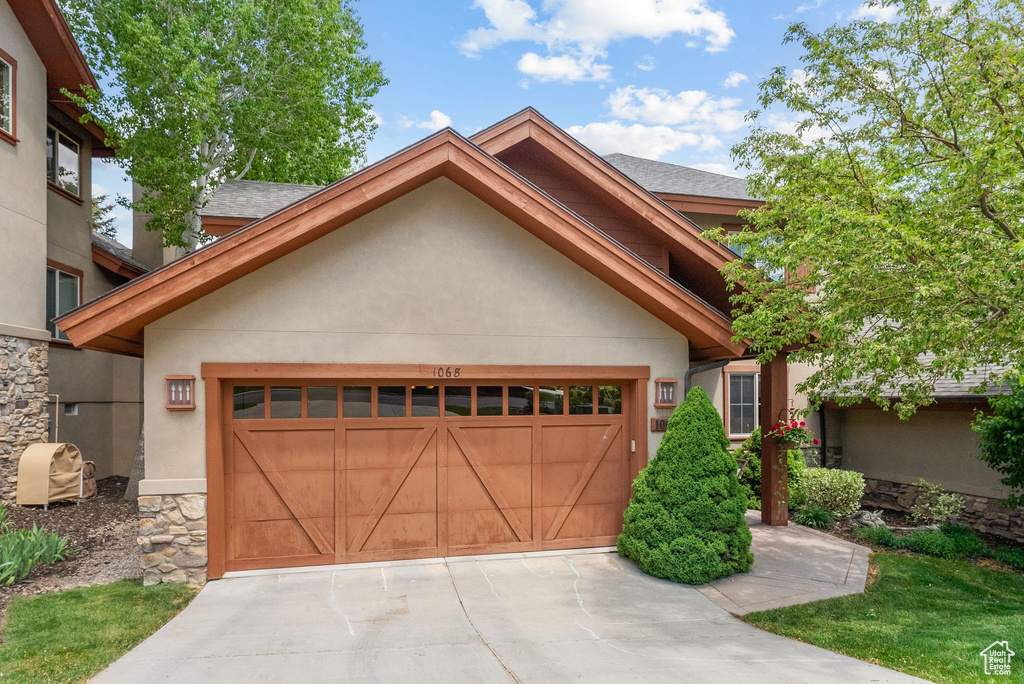 View of front of house featuring an attached garage, stucco siding, driveway, and stone siding
