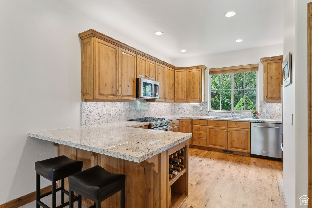 Kitchen with appliances with stainless steel finishes, a peninsula, tasteful backsplash, recessed lighting, and light wood-style flooring