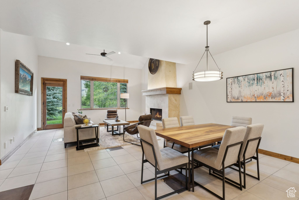 Dining space featuring a lit fireplace, baseboards, light tile patterned floors, and ceiling fan