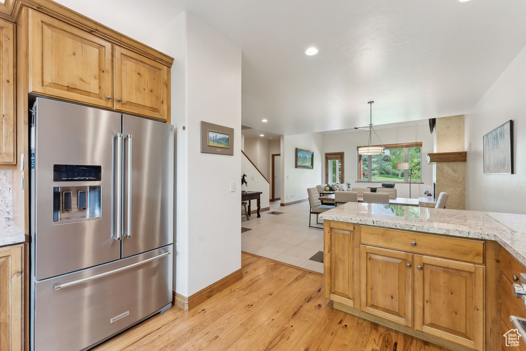 Kitchen featuring high end refrigerator, light wood-style flooring, open floor plan, light stone countertops, and recessed lighting