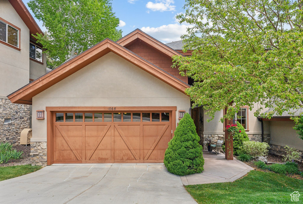 View of front of home with stone siding, stucco siding, concrete driveway, and an attached garage