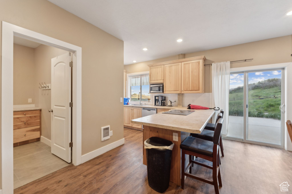 Kitchen featuring light brown cabinets, stainless steel appliances, light countertops, a breakfast bar area, and light wood-style floors