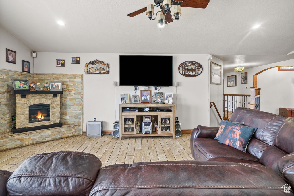 Living room featuring a ceiling fan, wood finished floors, a stone fireplace, baseboards, and arched walkways
