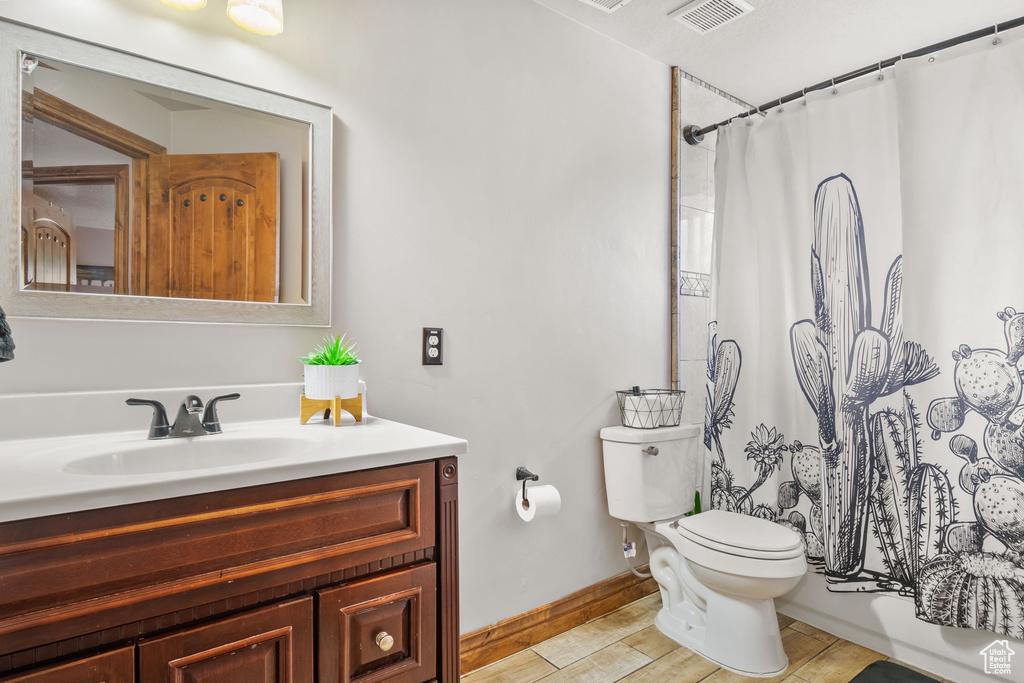 Bathroom with toilet, baseboards, vanity, curtained shower, and wood finished floors