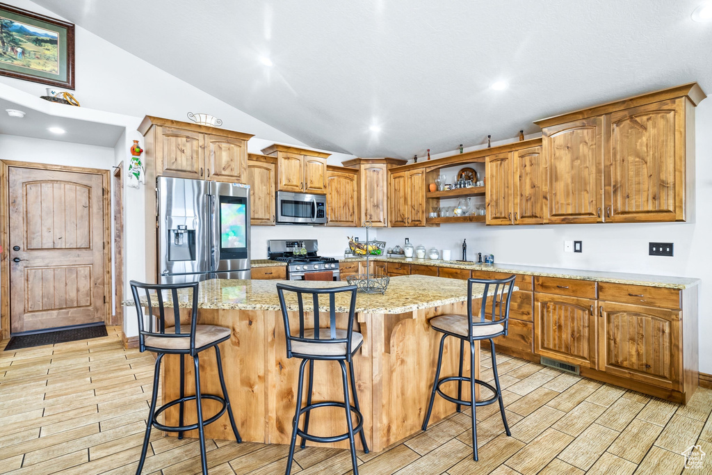 Kitchen with appliances with stainless steel finishes, vaulted ceiling, open shelves, wood tiled floors, and brown cabinets