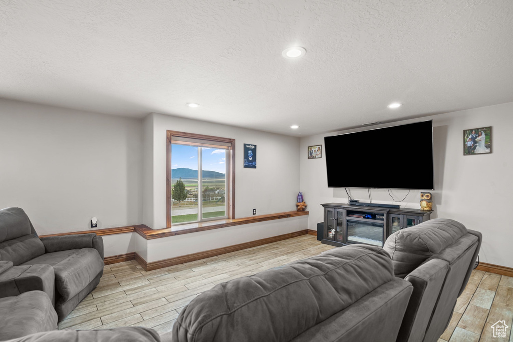 Living room featuring light wood-type flooring, baseboards, a textured ceiling, and recessed lighting