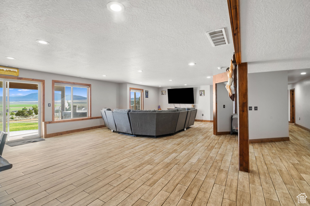 Living room featuring a textured ceiling, baseboards, light wood-style flooring, and recessed lighting