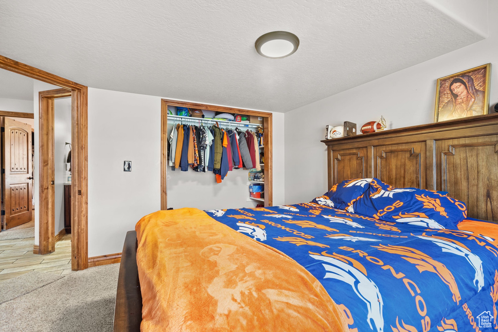 Bedroom with light carpet, a closet, and a textured ceiling