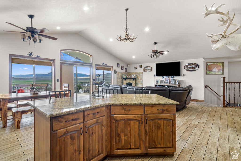 Kitchen featuring ceiling fan, light wood finished floors, a fireplace, light stone countertops, and a kitchen island