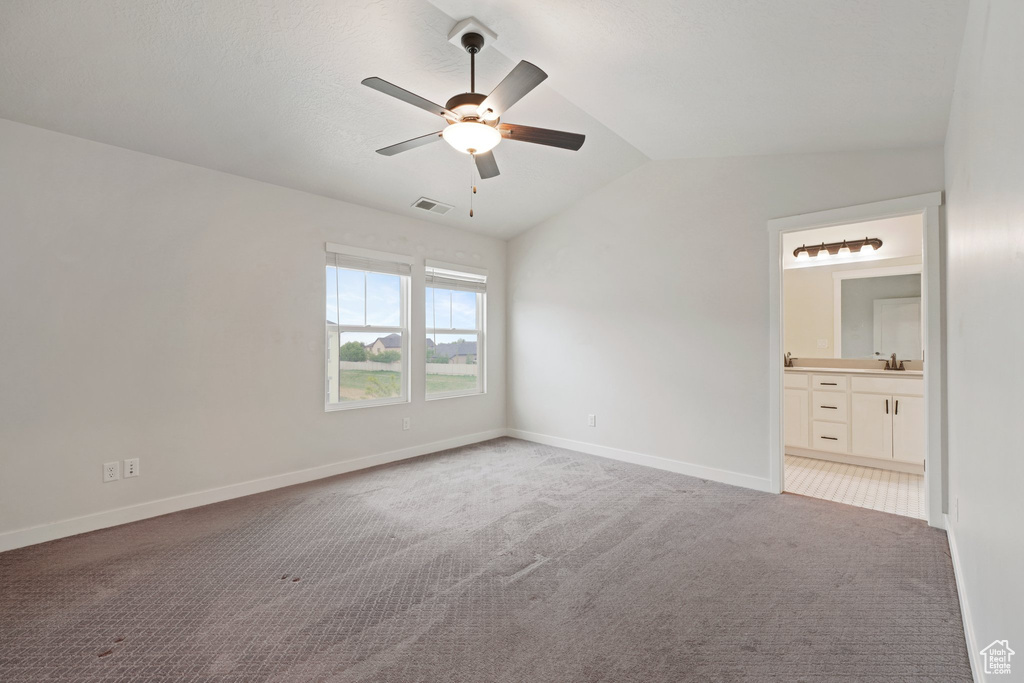 Unfurnished bedroom featuring light colored carpet, vaulted ceiling, baseboards, ensuite bath, and ceiling fan
