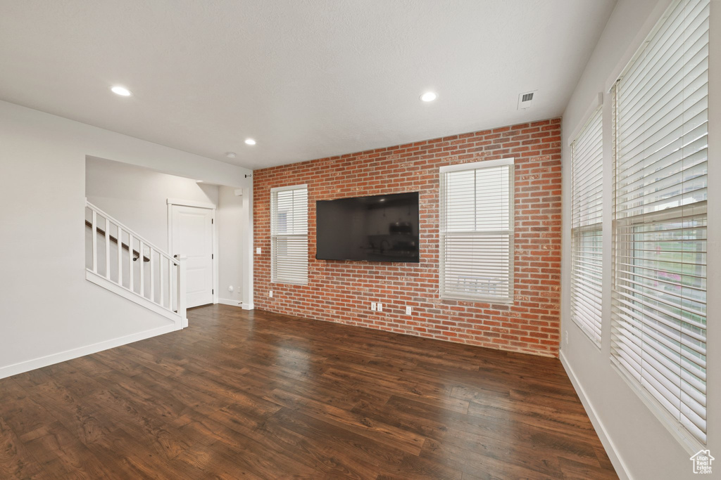 Unfurnished living room featuring brick wall, stairs, dark wood-type flooring, baseboards, and recessed lighting