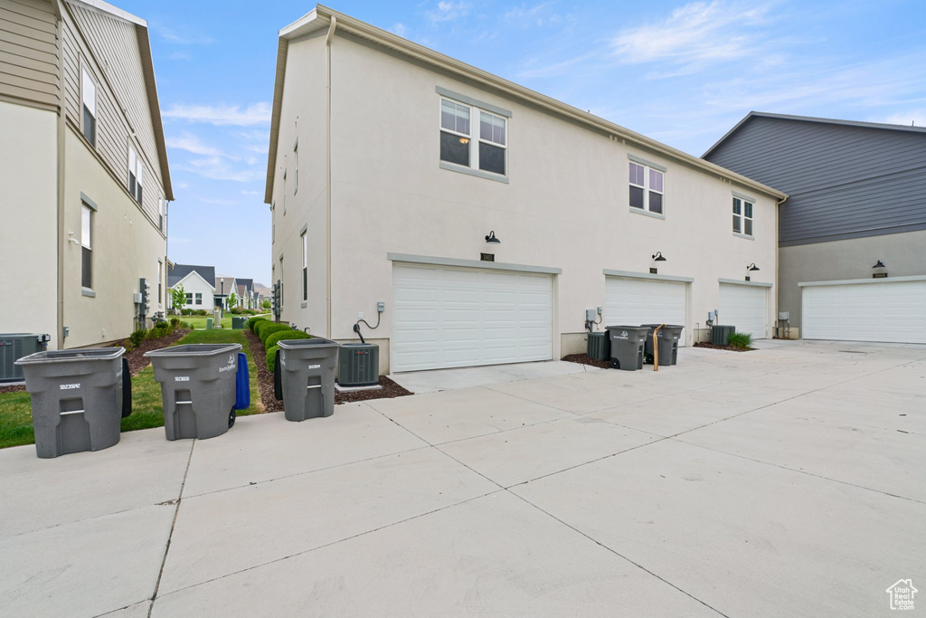 Rear view of property featuring stucco siding, concrete driveway, an attached garage, and central AC