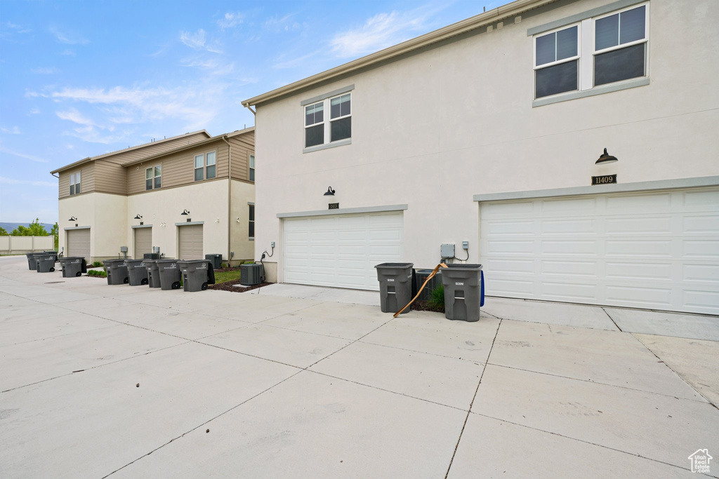 Back of property featuring stucco siding, central AC, a garage, and driveway