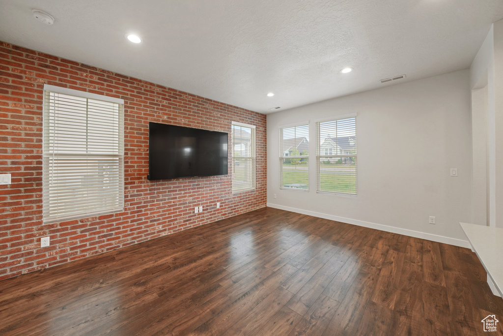 Unfurnished living room with brick wall, wood finished floors, baseboards, recessed lighting, and a textured ceiling