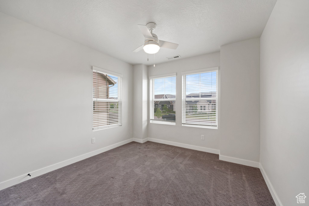 Empty room featuring dark colored carpet, a ceiling fan, baseboards, and a textured ceiling