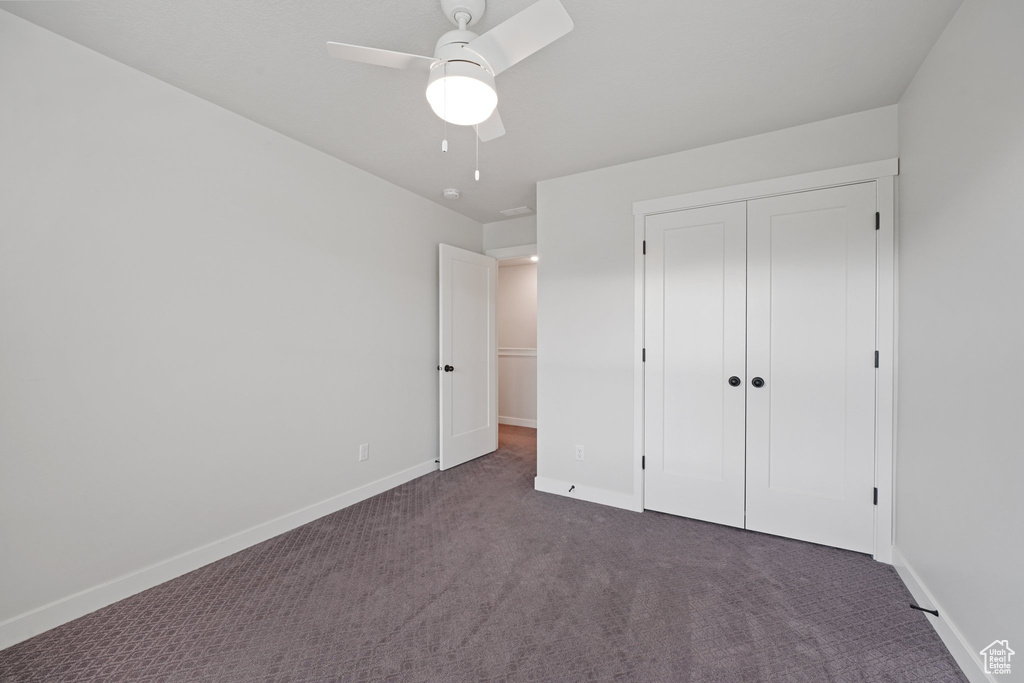 Unfurnished bedroom with dark colored carpet, baseboards, a closet, and a ceiling fan