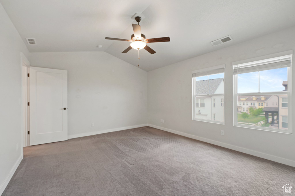Empty room featuring carpet, a ceiling fan, baseboards, and vaulted ceiling
