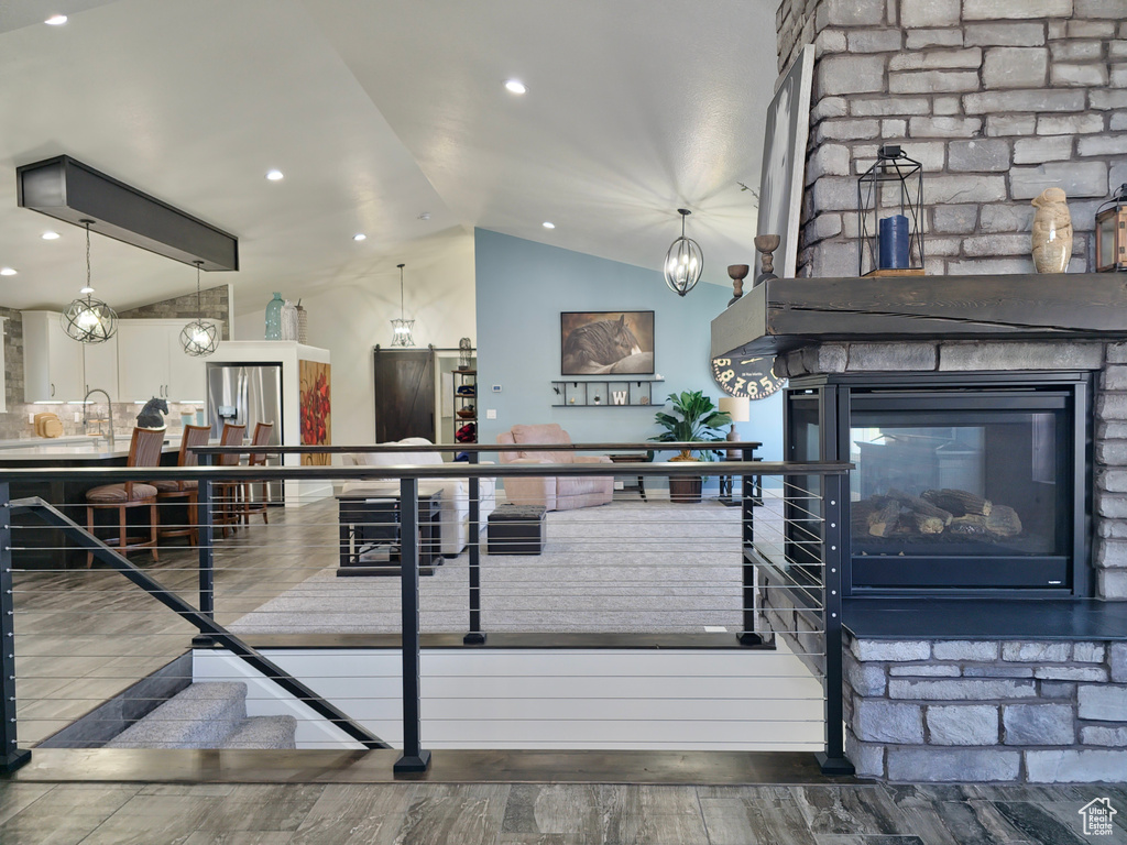 Living area with vaulted ceiling, a stone fireplace, and wood finished floors