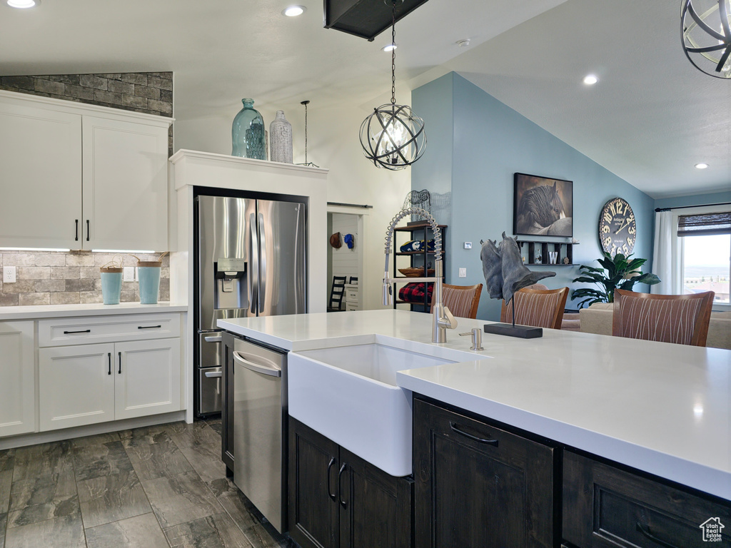 Kitchen with vaulted ceiling, appliances with stainless steel finishes, a sink, white cabinets, and light countertops