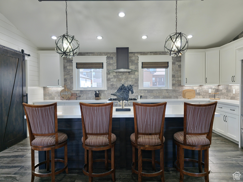 Kitchen featuring wall chimney exhaust hood, healthy amount of natural light, backsplash, an island with sink, and recessed lighting