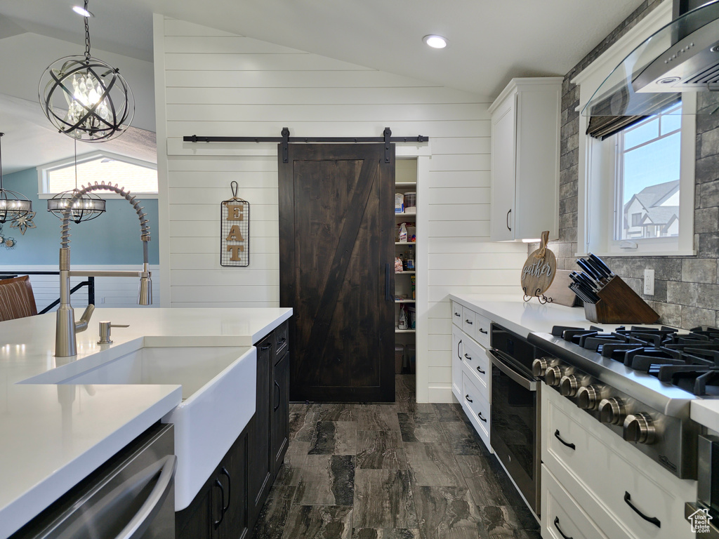 Kitchen with vaulted ceiling, stainless steel appliances, a sink, a barn door, and white cabinetry