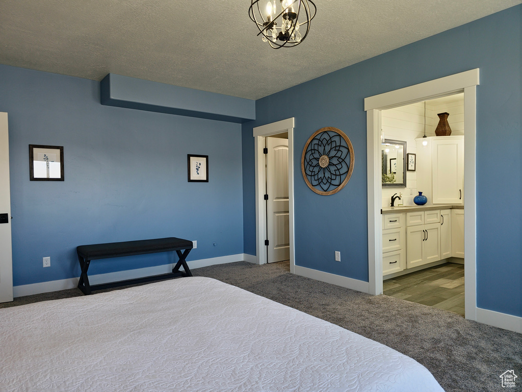 Bedroom with dark carpet, a chandelier, baseboards, a textured ceiling, and ensuite bath