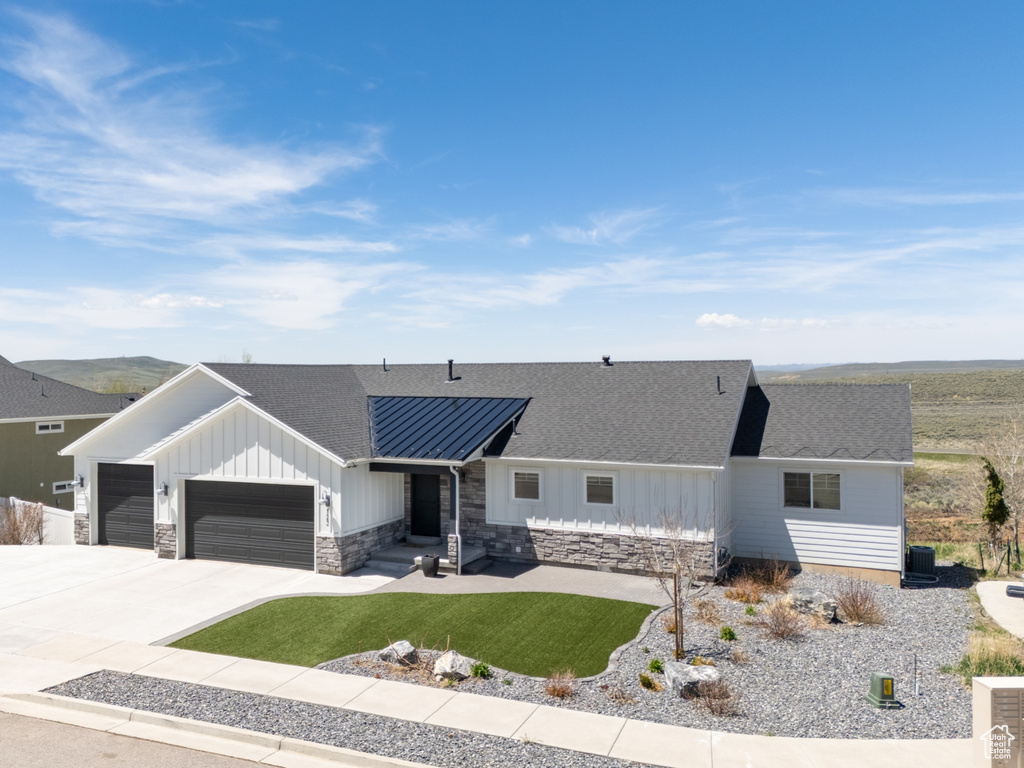 View of front facade with an attached garage, stone siding, board and batten siding, concrete driveway, and a front lawn