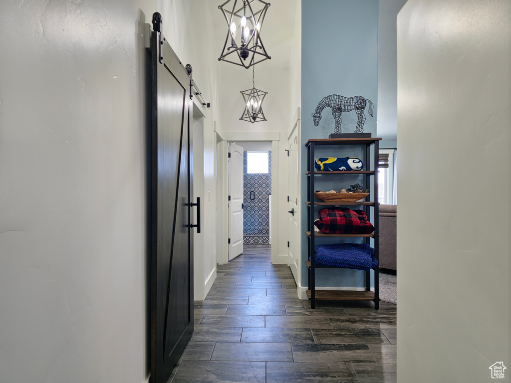 Hallway featuring a barn door, a chandelier, dark wood finished floors, baseboards, and a towering ceiling