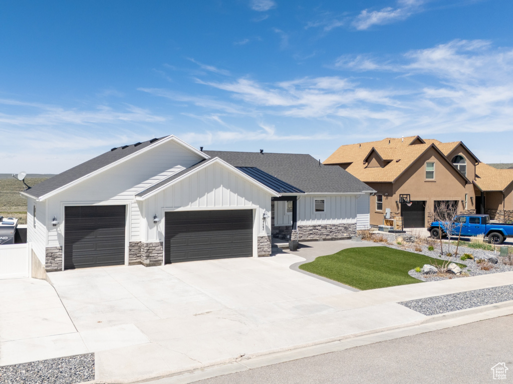 View of front facade with a garage, board and batten siding, fence, concrete driveway, and stone siding