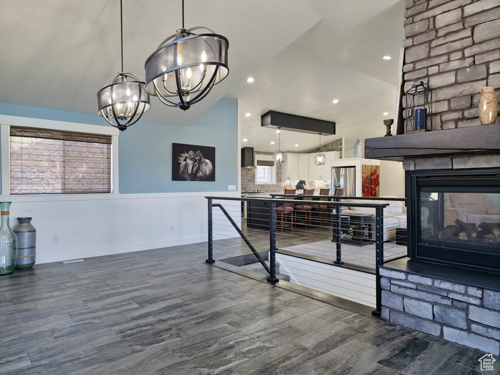 Recreation room featuring a chandelier, dark wood-type flooring, lofted ceiling, a stone fireplace, and wainscoting