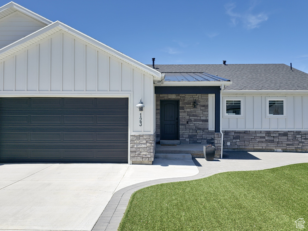 View of front facade with stone siding, a garage, board and batten siding, concrete driveway, and a shingled roof