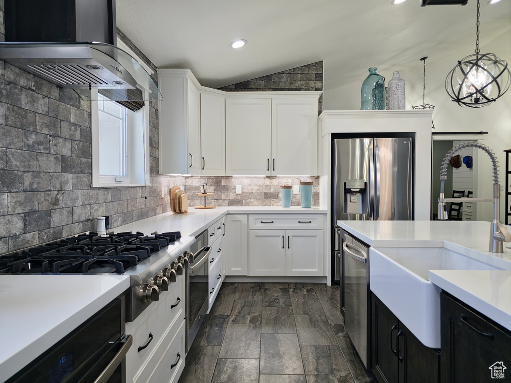 Kitchen with ventilation hood, lofted ceiling, appliances with stainless steel finishes, light countertops, and white cabinetry