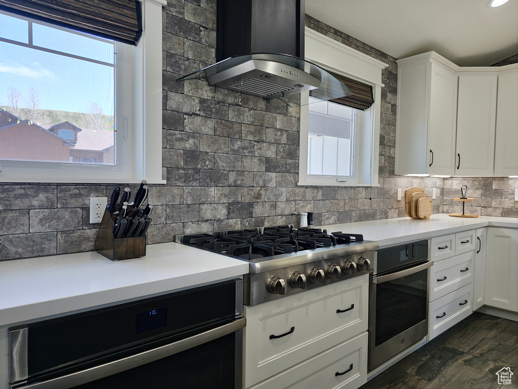 Kitchen featuring stainless steel appliances, wall chimney range hood, backsplash, and light countertops