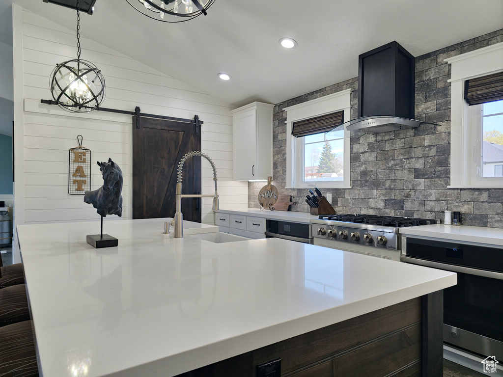 Kitchen with stainless steel appliances, wall chimney exhaust hood, light countertops, vaulted ceiling, and tasteful backsplash
