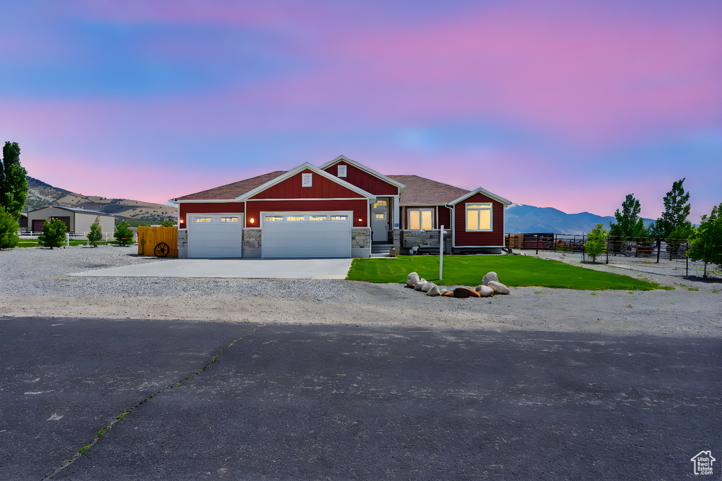 Single story home featuring an attached garage, driveway, a mountain view, and stone siding