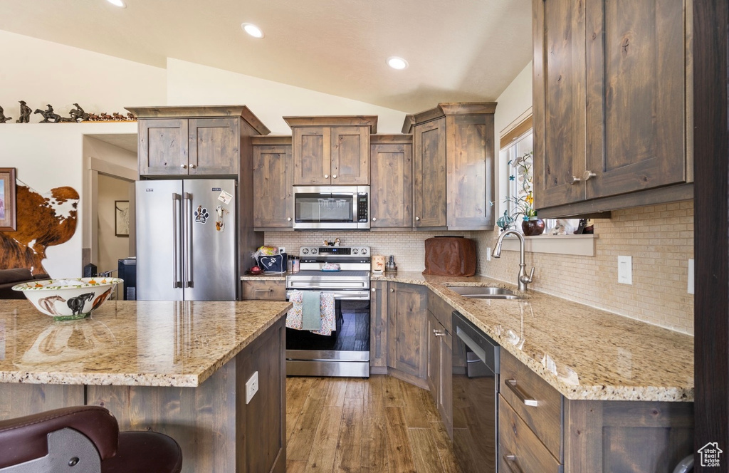 Kitchen featuring stainless steel appliances, a sink, vaulted ceiling, wood finished floors, and backsplash