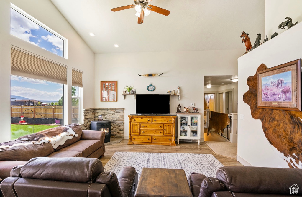 Living room featuring a ceiling fan, a wood stove, wood finished floors, high vaulted ceiling, and recessed lighting
