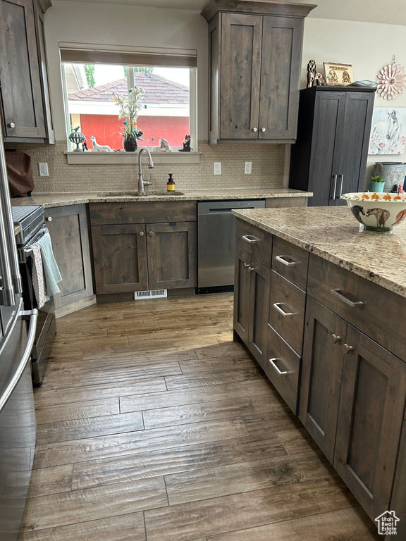 Kitchen with appliances with stainless steel finishes, a sink, tasteful backsplash, dark wood-style flooring, and light stone countertops