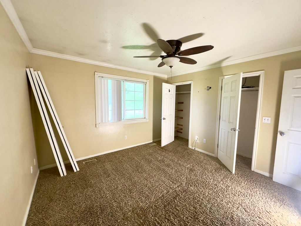 Unfurnished bedroom featuring dark carpet, ornamental molding, multiple closets, baseboards, and a ceiling fan