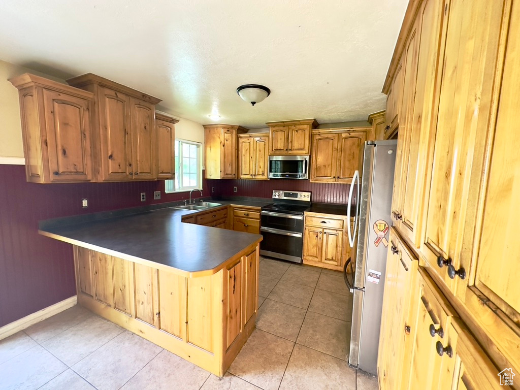 Kitchen with appliances with stainless steel finishes, a sink, a peninsula, dark countertops, and light tile patterned floors