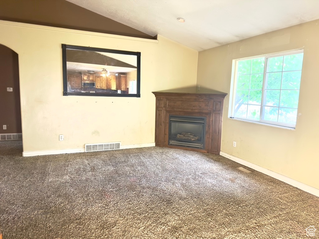 Unfurnished living room with lofted ceiling, a glass covered fireplace, arched walkways, carpet flooring, and baseboards